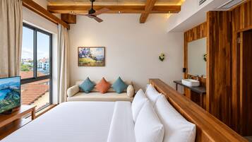 Een hotelkamer met een groot bed, een houten bankje, een televisie, een schilderij en uitzicht op buiten.