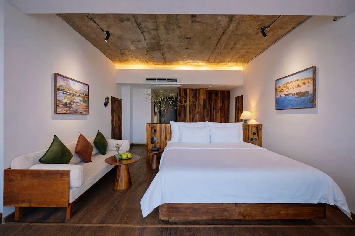 A modern hotel room with a large bed, a sofa, wooden accents, and artwork on the walls.