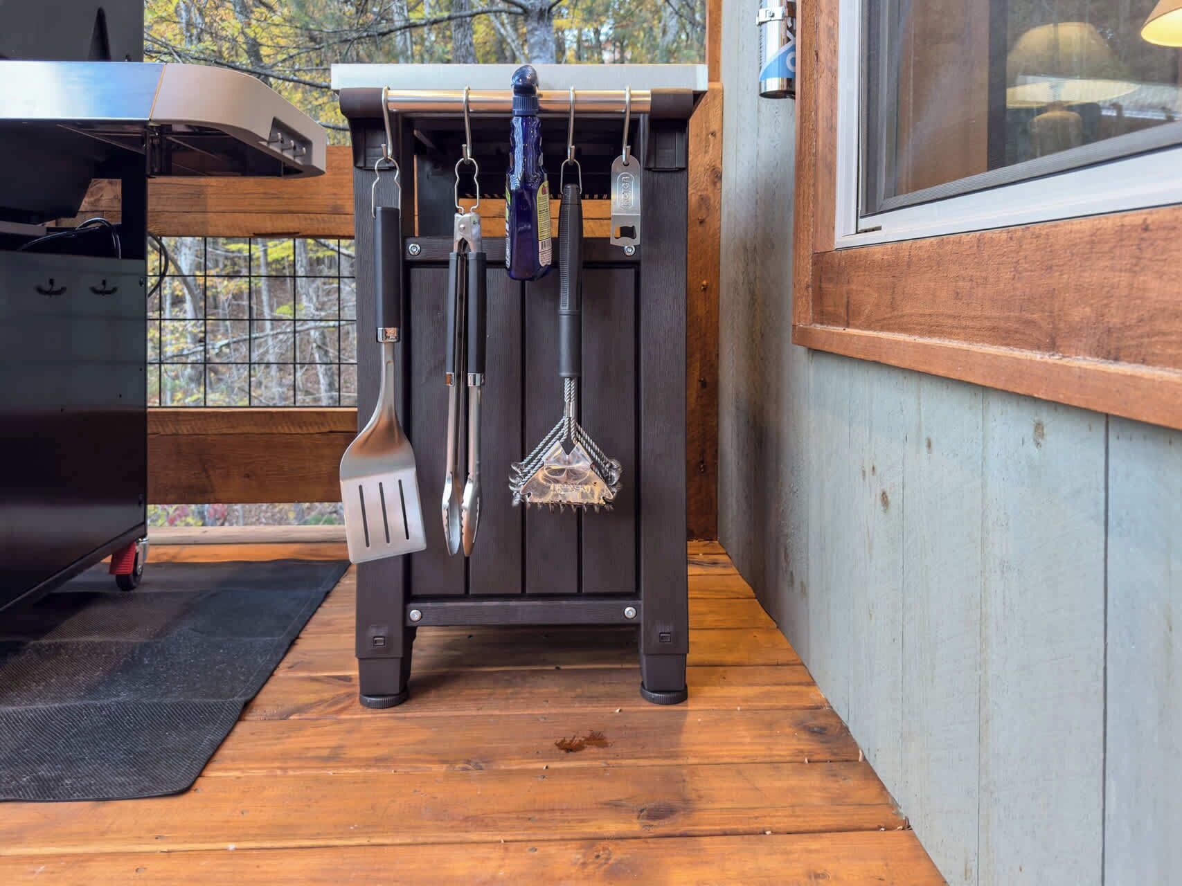 Een keuken met een ingebouwde grill, hangend keukengerei en een raam met uitzicht op bomen.