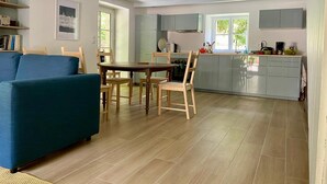 A modern kitchen with grey cabinets, a dining area with a wooden table and chairs, and a blue sofa in the living room. - Manoir du Menez Bihan - The refurbished gite - Site overlooking the Bay of Audierne (Audierne)