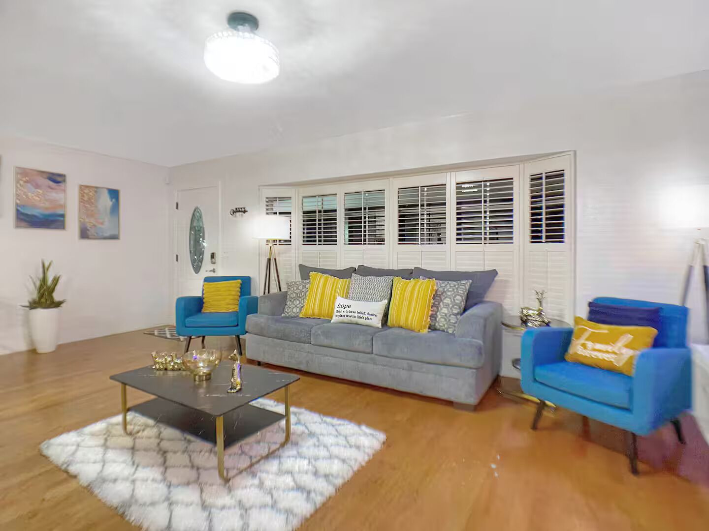 Ein Wohnzimmer mit grauem Sofa, blauen Sesseln, einem Couchtisch und einem weißen Teppich.