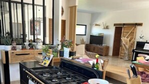 Una cocina moderna con una estufa grande, un comedor con una mesa de madera y una sala de estar con televisión y adornos.