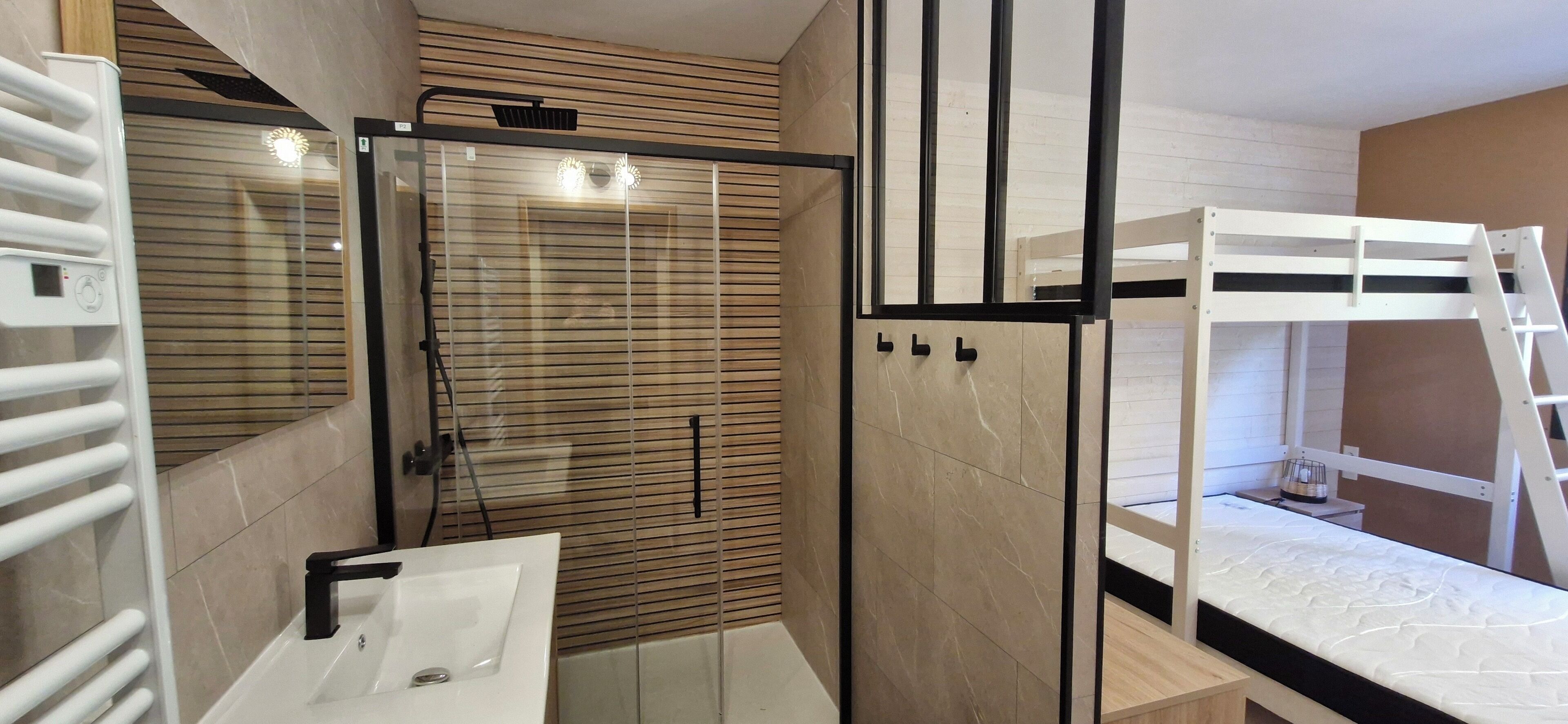 Une salle de bain moderne avec une douche à parois de verre, un lavabo blanc et un lit superposé avec une échelle.