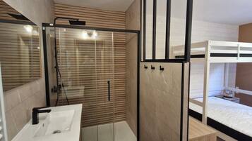 Une salle de bain moderne avec une douche à parois de verre, un lavabo blanc et un lit superposé avec une échelle.
