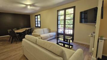 A modern living room with a sofa, a dining table with chairs, and a TV mounted on the wall.