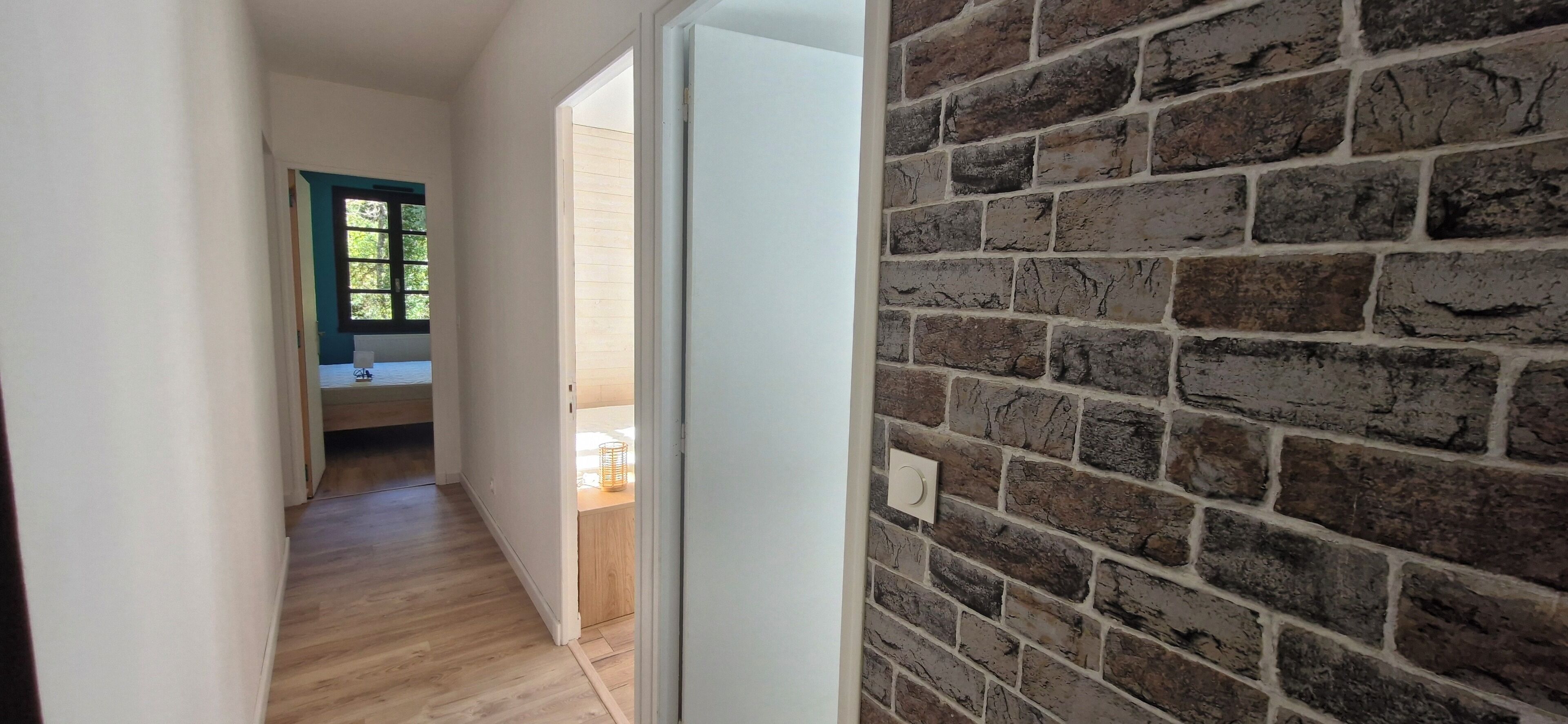 Un couloir avec un plancher en bois, une porte blanche et un mur en briques.