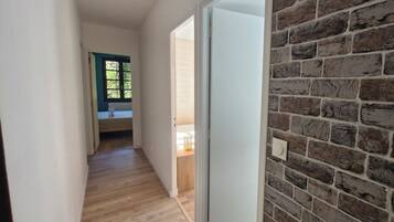 Un couloir avec un plancher en bois, une porte blanche et un mur en briques.