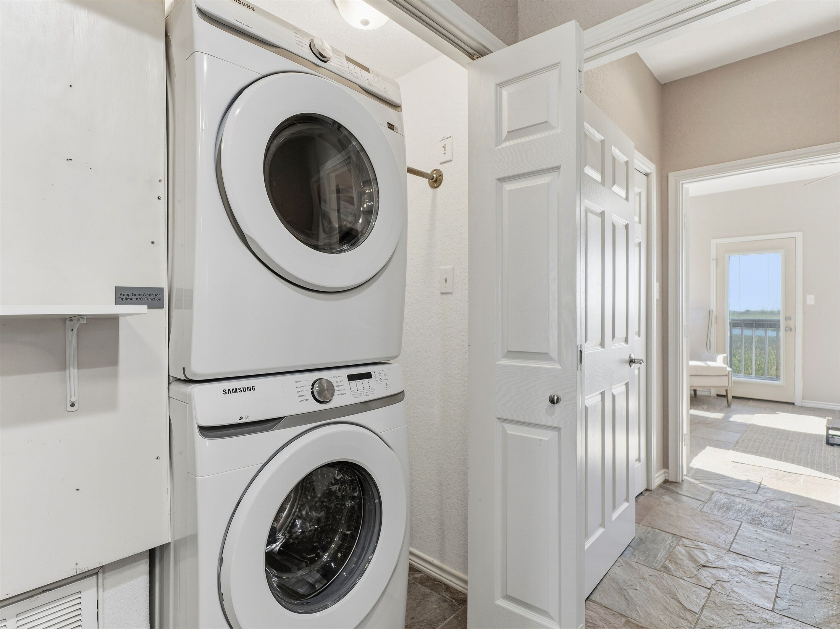 A laundry room with stacked washers and dryers, a door leading to a balcony, and a tiled floor.