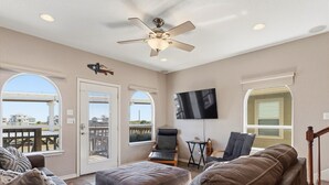 Un ampio soggiorno con ventilatore a soffitto, televisore a schermo piatto e vista sulla spiaggia tramite ampie finestre.
