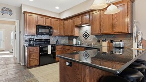 Una cucina moderna con mobili in legno, un forno a microonde nero, un piano cottura e una grande isola con sgabelli da bar.