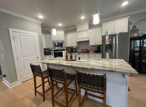 A modern kitchen with white cabinets, a granite countertop, and a central island with bar stools. - Masters Week 2026 Rental-Brand new home - 9 miles from the Augusta National. (Graniteville)