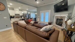 Ein geräumiges Wohnzimmer mit einer großen Eckcouch, einem Kamin und einem an der Wand befestigten Fernseher.