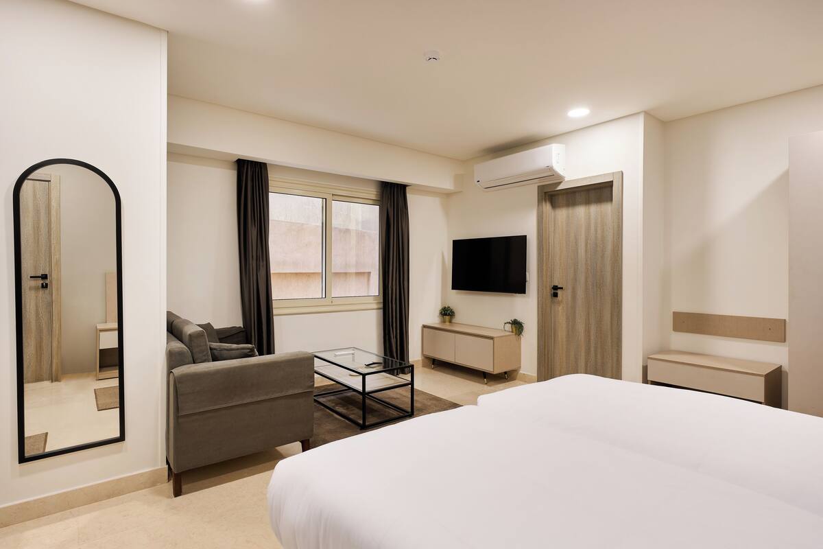A modern hotel room with a bed, a sofa, a TV, a wardrobe, and a window with curtains.