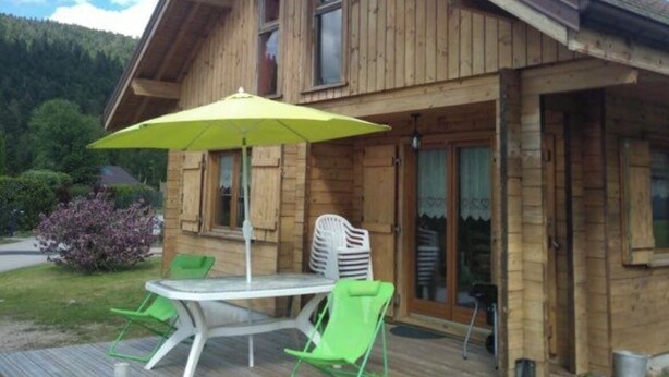 A wooden cabin with a deck, a table with chairs, and a yellow umbrella. - Cosy chalet 2-8pers/linen provided (Gérardmer)