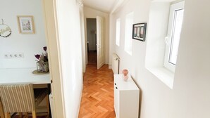A hallway with a wooden floor, a white desk with a chair, a white cabinet, and a window. - Vintage Loft in the center (Cluj-Napoca)