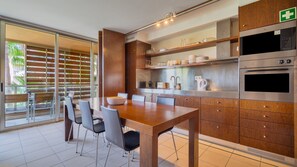 A modern kitchen with wooden cabinets, stainless steel appliances, and a dining area with a large table and chairs. - T2 Estiloso c/ Piscina nos Salgados by LovelyStay (Vale Rebelho)
