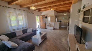 A modern living room with a dark grey sofa, a white coffee table, and a TV on a wooden stand. A kitchen is visible in the background with wooden cabinets and a dining area. - Villa Edo beautiful built villa with private pool in a small village in Istria (ZMINJ)