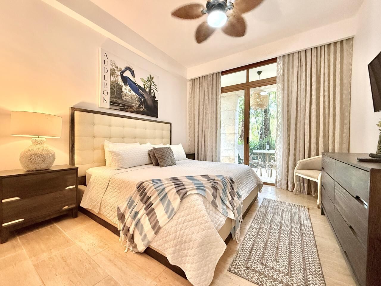 Une chambre à coucher moderne avec un grand lit, une table de chevet, une commode et un ventilateur de plafond.