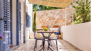 Een terras met een tafel en stoelen, een stenen muur en een deur met blauwe luiken.