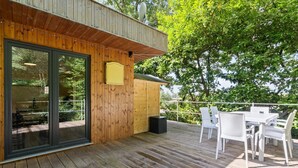 Una terraza de madera con mobiliario exterior y un ventanal que da a un espacio interior.