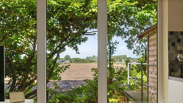Vista desde una habitación con ventana que da a un campo y un edificio a lo lejos.