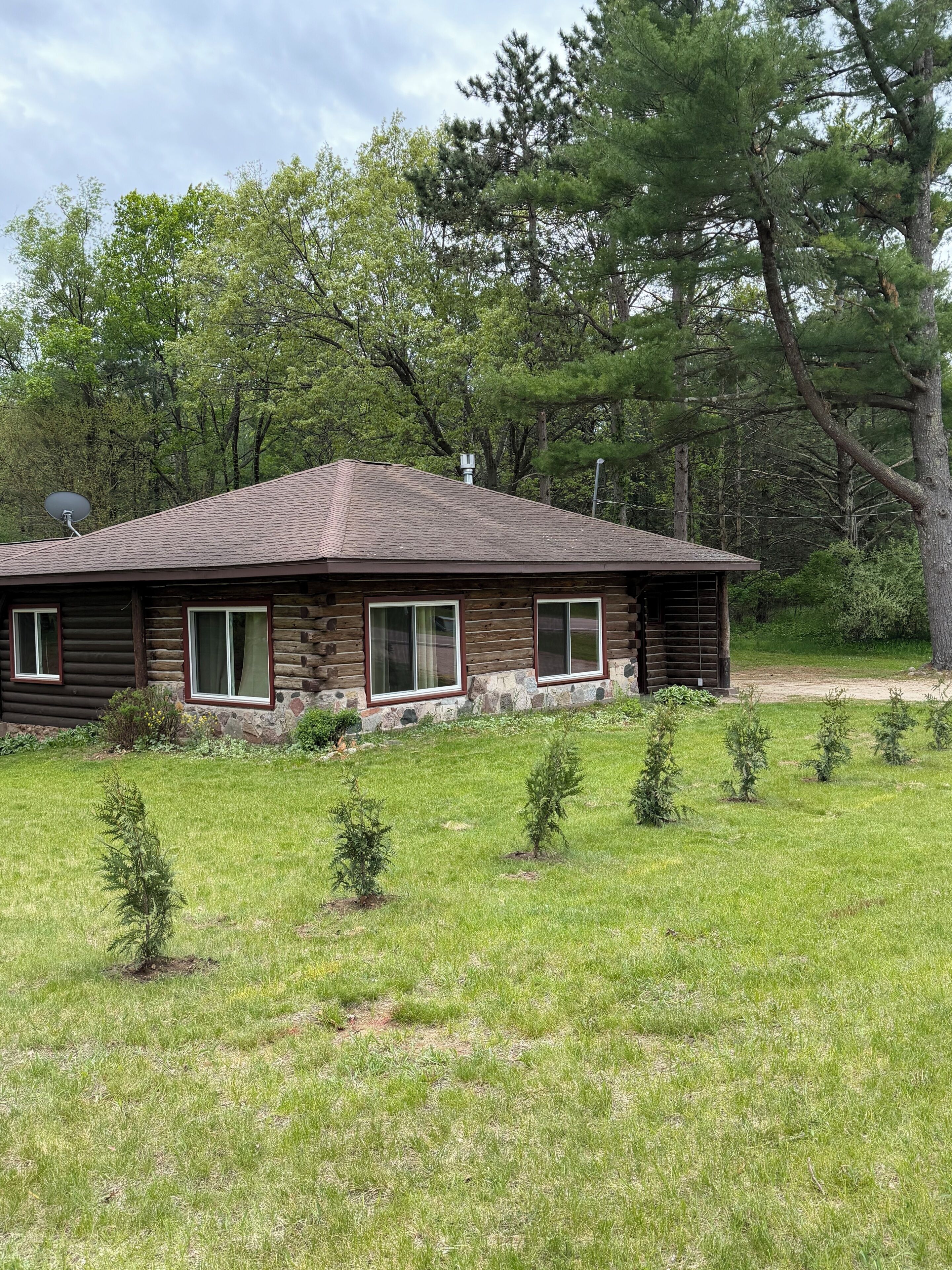 A log cabin with a sloped roof, surrounded by a grassy yard and small trees.