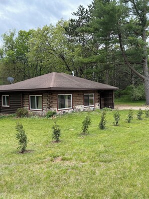 A log cabin with a sloped roof, surrounded by a grassy yard and small trees. - Cabin Retreat in Mount Morris (Wild Rose)