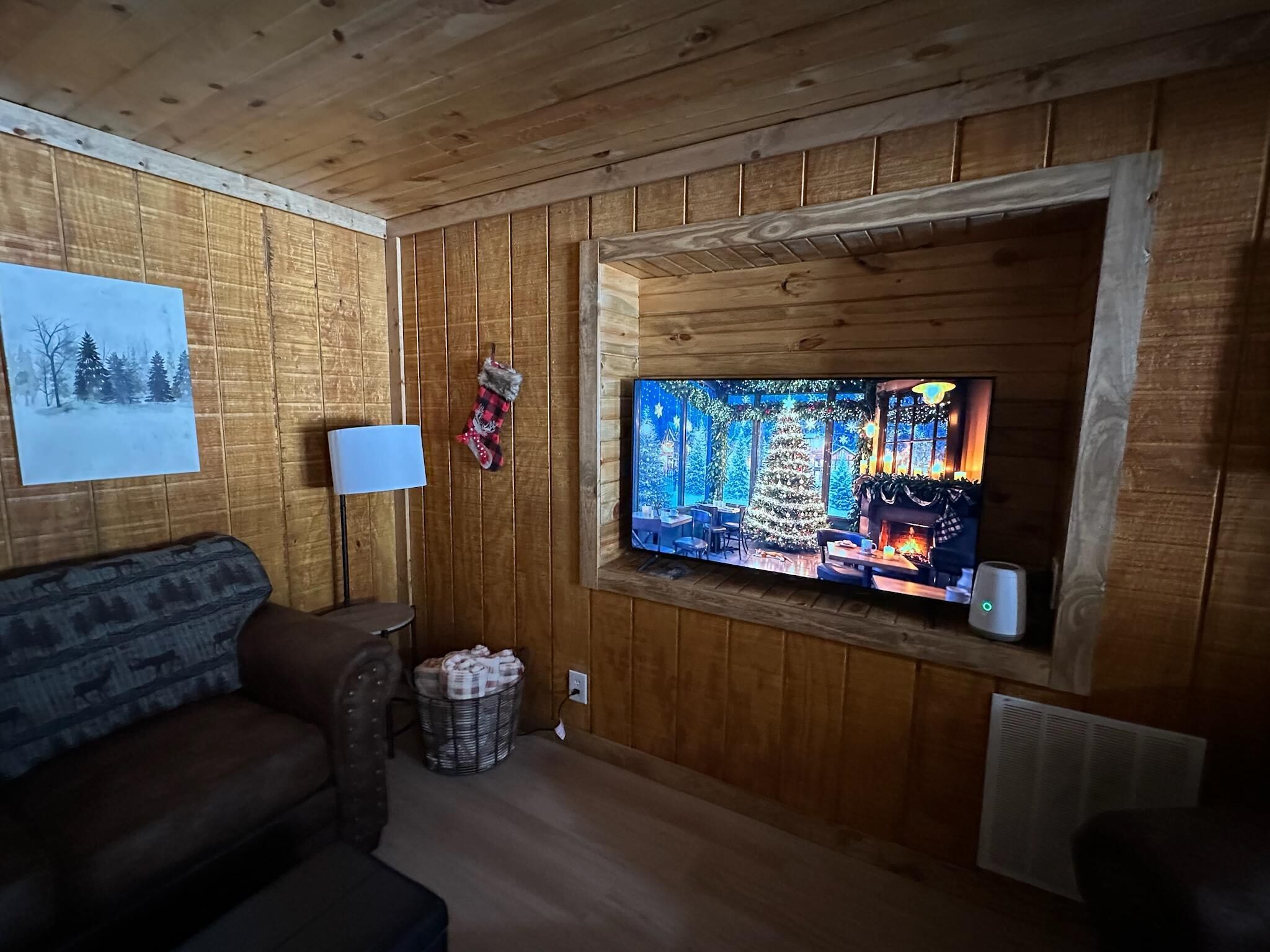Une pièce chaleureuse avec des murs en bois, un téléviseur fixé au mur, un canapé et une cheminée.
