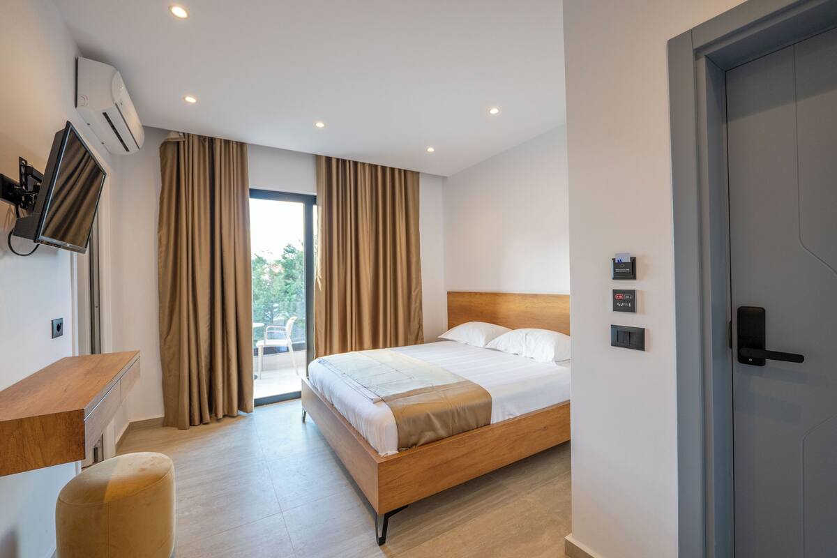 Habitació d'hotel moderna amb un llit de fusta, un escriptori i una finestra gran amb cortines.