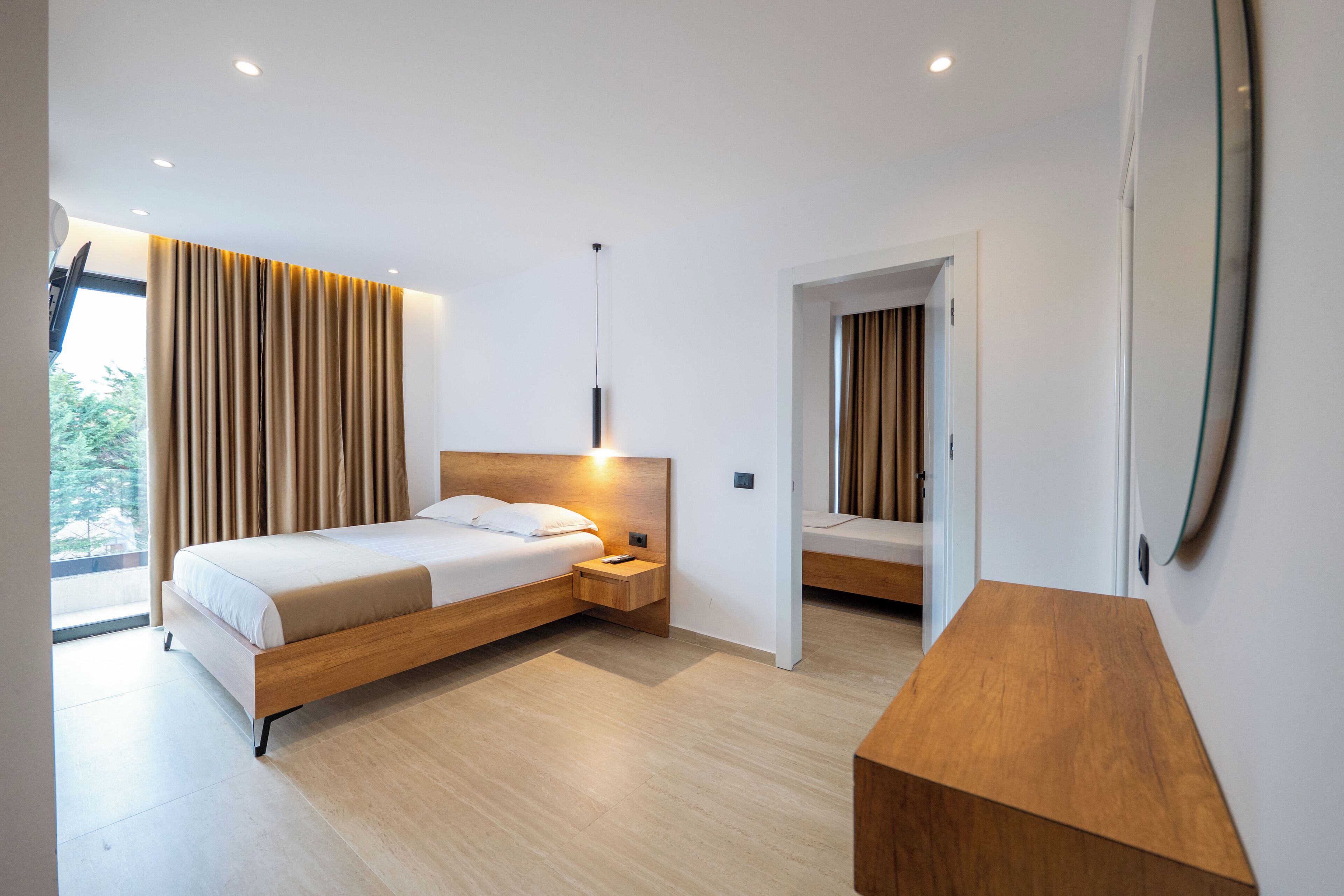 A modern bedroom with a wooden bed, bedside tables, a nightstand, and a large window with curtains.