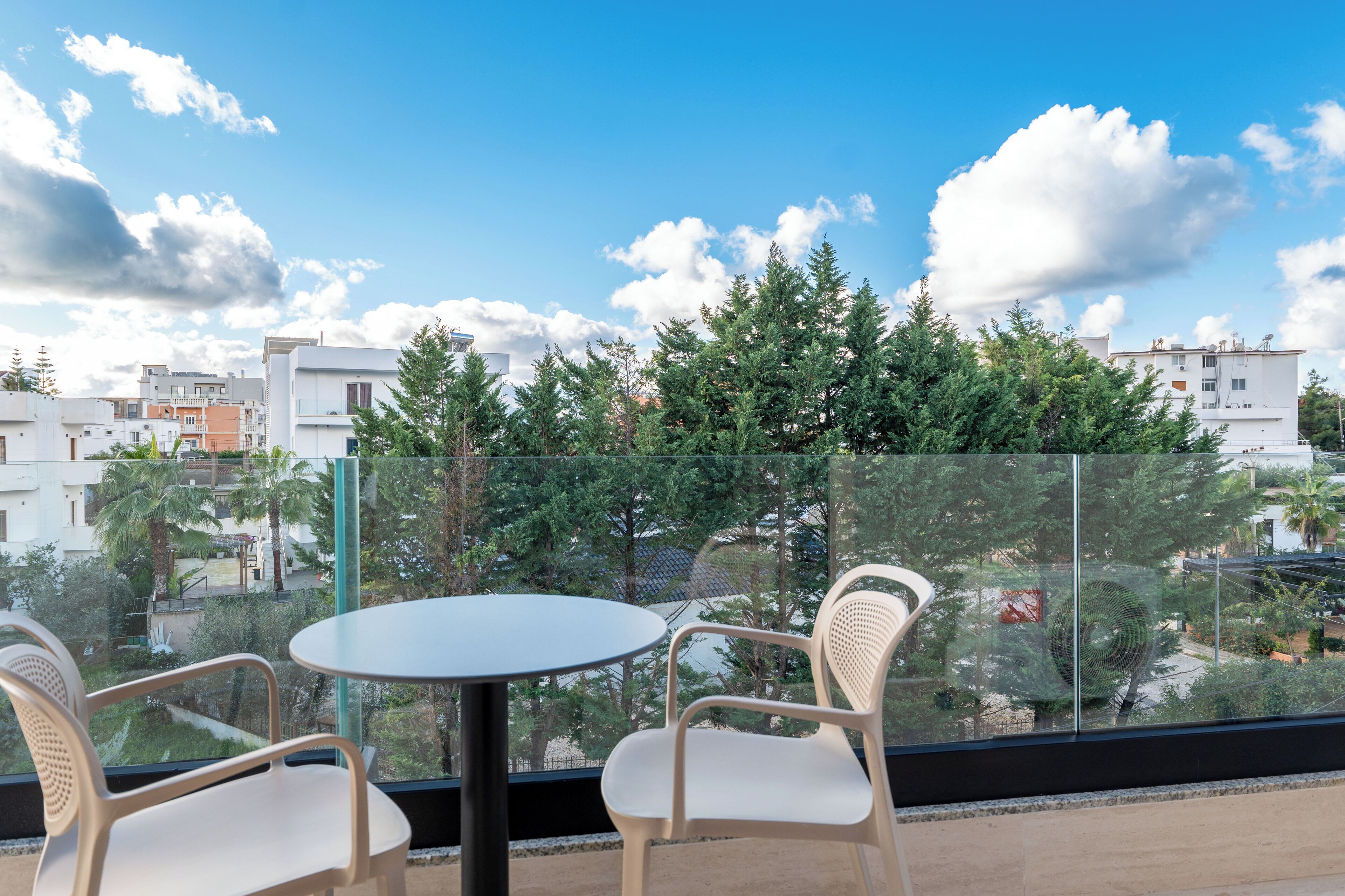 A balcony with a glass railing, two white chairs, and a round table.