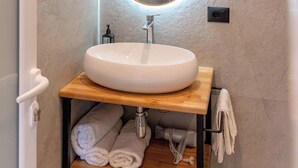 A bathroom with a round mirror, white sink, wooden vanity, and towels. - Hotel ENAD (Ksamil)