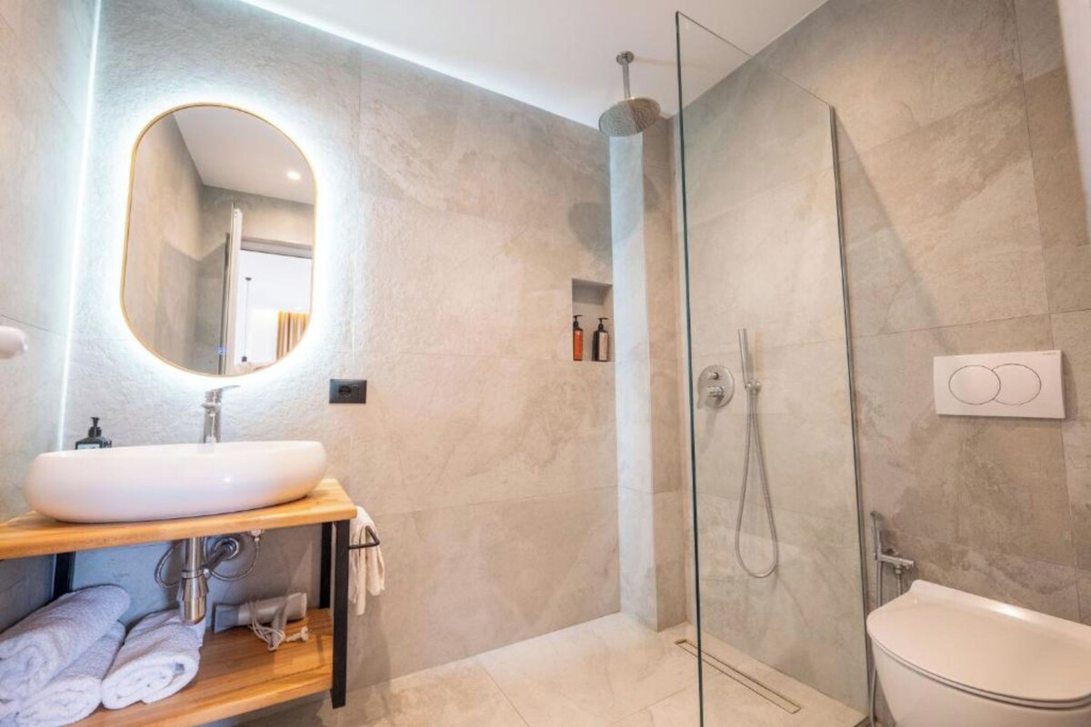 A modern bathroom with a glass-enclosed shower, a white sink, and a mirror with a gold frame.