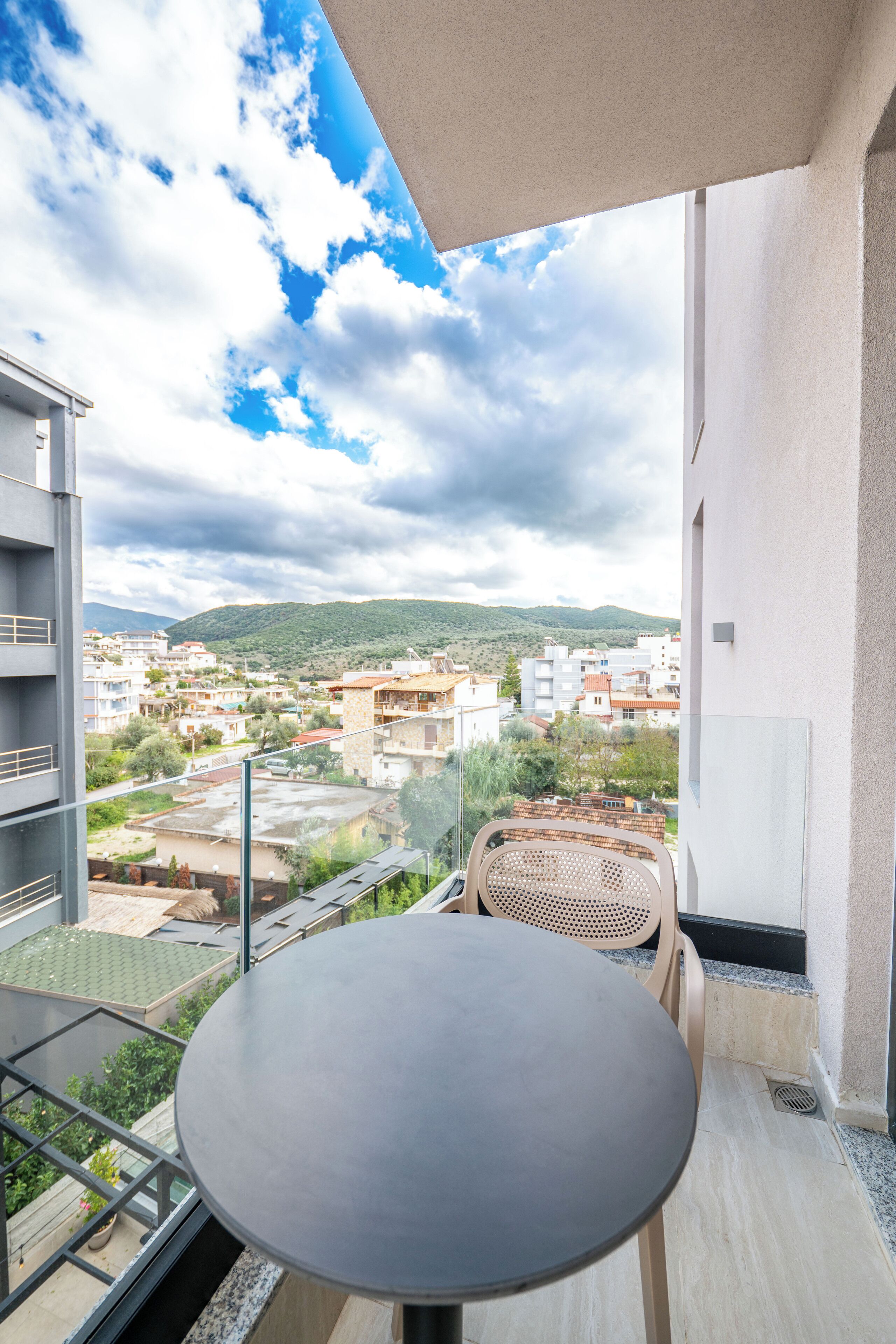 Un balcone con tavolo e sedie, vista su una zona residenziale con edifici e colline.