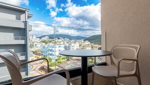 A balcony with two chairs and a table, overlooking a cityscape with buildings and mountains. - Hotel ENAD (Ksamil)