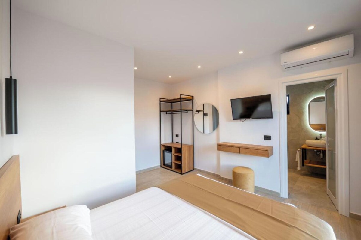 A modern bedroom with a large bed, a TV mounted on the wall, a built-in wardrobe, and an air conditioning unit.