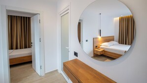 A modern hotel room with a wooden bed, a bedside table, a mirror, and a door leading to a bathroom. - Hotel ENAD (Ksamil)