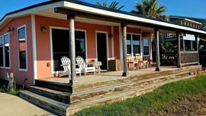 A pink house with a porch, white chairs, and a wooden deck. - Home, Hooks & Heart: Anglers Paradise Family-Friendly Bay House Marina 2 Blocks (Corpus Christi)