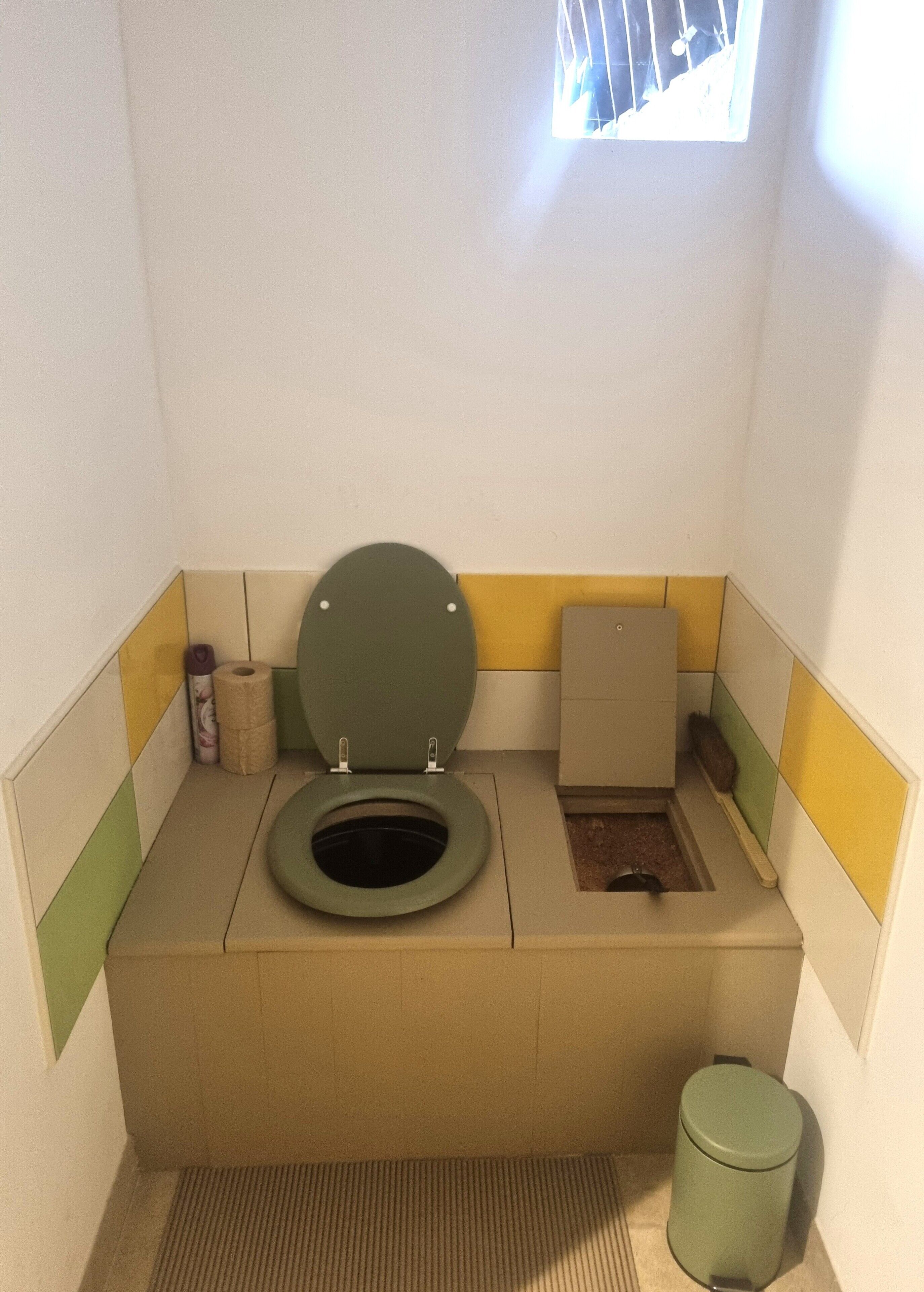 Een kleine badkamer met toilet, prullenbak en een klein raam.