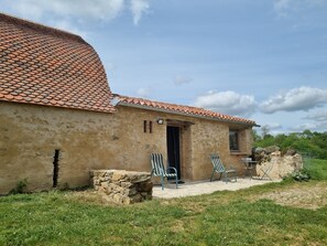 A rustic building with a tiled roof, a stone wall, and two outdoor chairs.