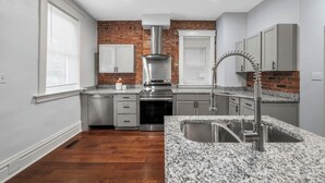 Een moderne keuken met granieten aanrechtbladen, roestvrijstalen apparatuur en een wand van baksteen.