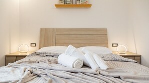 A neatly made bed with a wooden headboard, two bedside tables with illuminated lamps, and a shelf above the bed. - Comfortable Villa monni 1 for up to 2 guests (Arbatax)