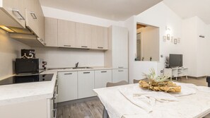 A modern kitchen with white cabinetry, a built-in microwave, and a dining area with a table set for two. - Comfortable Villa monni 1 for up to 2 guests (Arbatax)