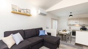A modern living room with a sectional sofa, a dining area with a table and chairs, and a kitchen with a microwave and stove. - Comfortable Villa monni 1 for up to 2 guests (Arbatax)