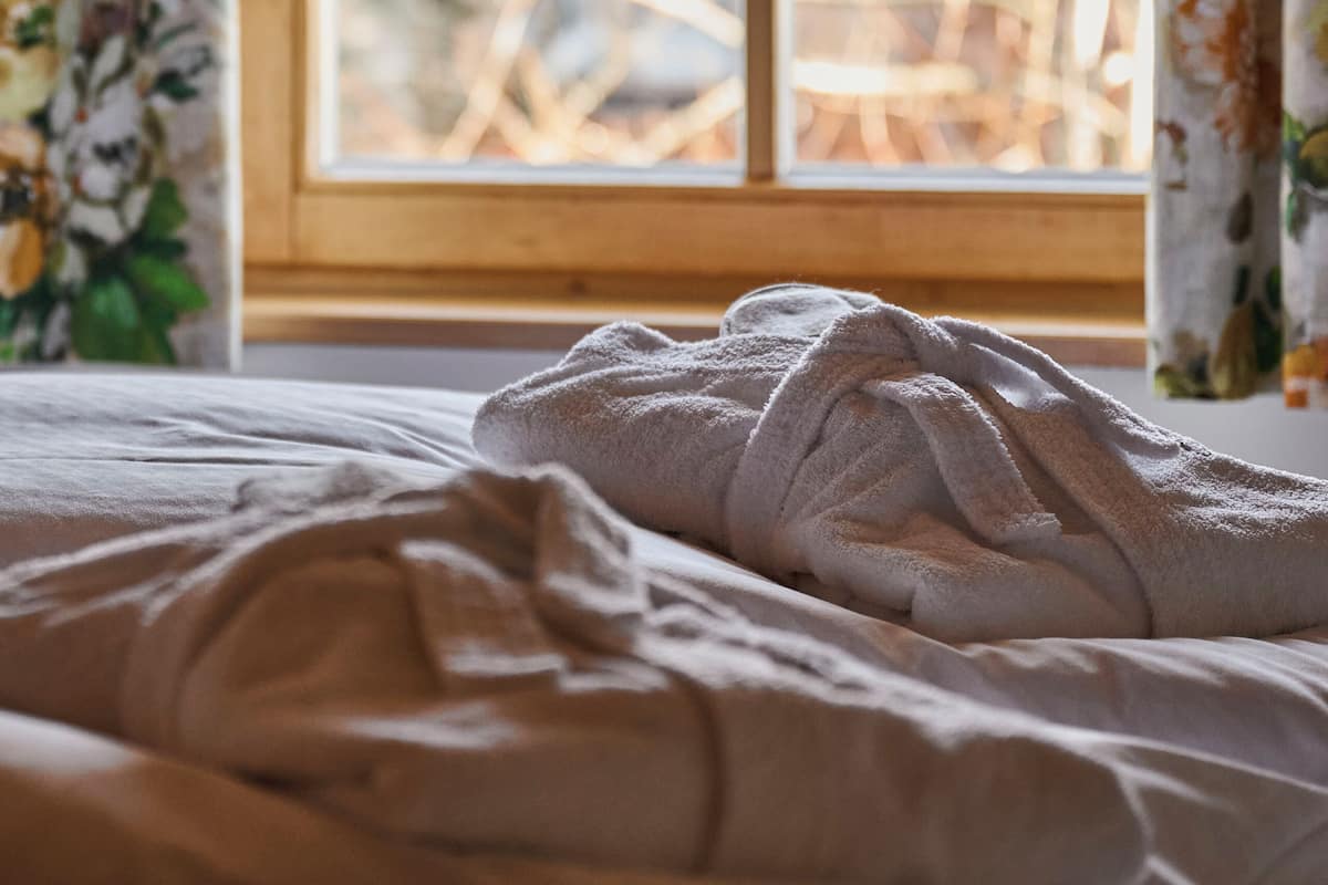 A bed with a white blanket, a window with a wooden frame, and floral curtains.