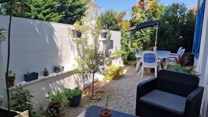 A patio area with a table and chairs, surrounded by potted plants and a white wall. - La Charmante (Puyoô)