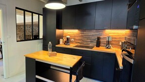 A modern kitchen with dark cabinets, a wooden countertop, and a built-in stove. - La Charmante (Puyoô)