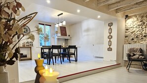 A modern living room with a dining area, a fireplace, and a stone wall. - La Charmante (Puyoô)
