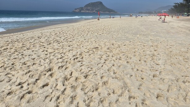 A wide sandy beach with footprints, a red flag, and a distant mountain.