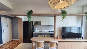 A modern kitchen with a dining area, featuring a large island, two chairs, a TV, and hanging plants.